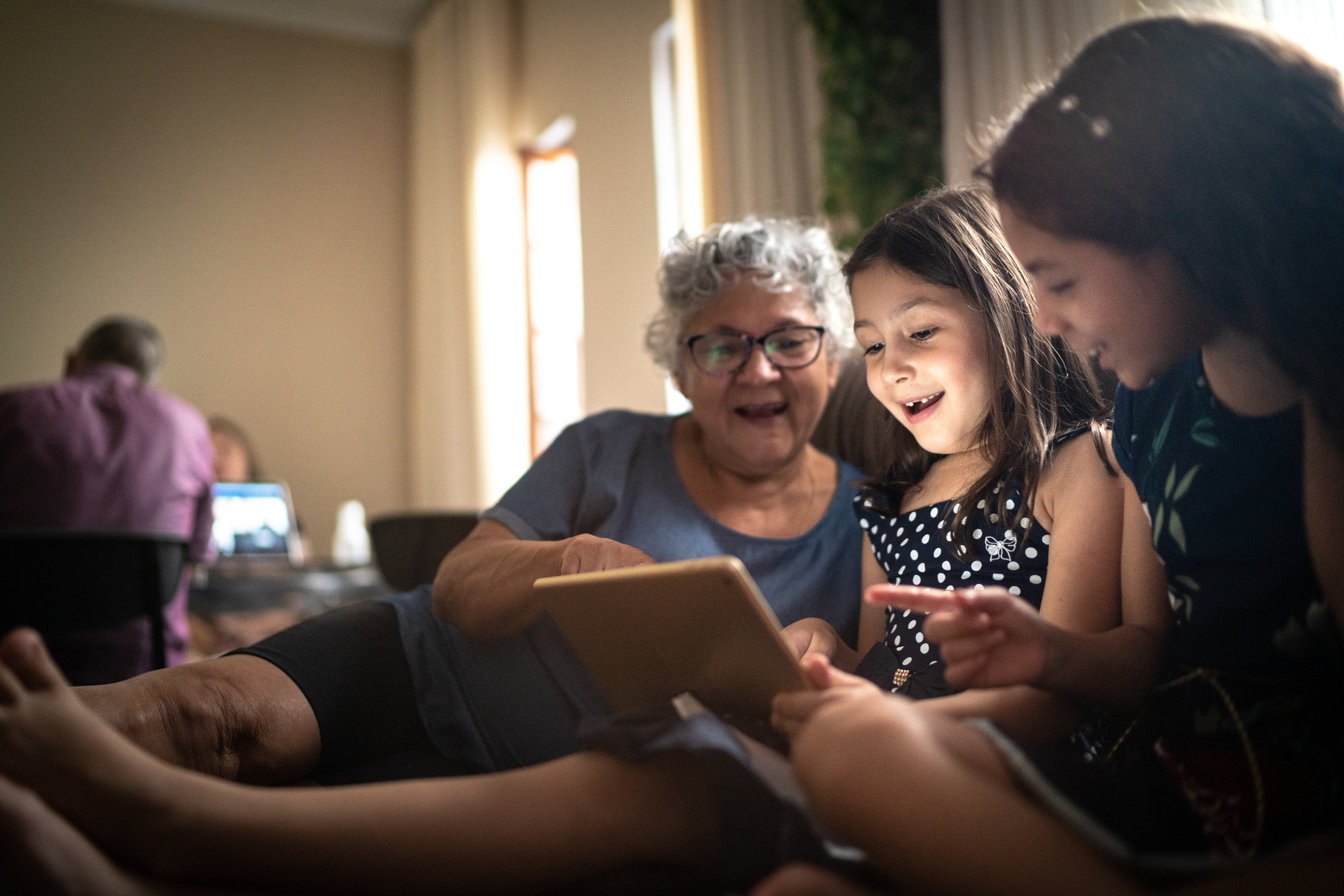 Photo of an older woman and two young girls looking at the screen of a tablet together